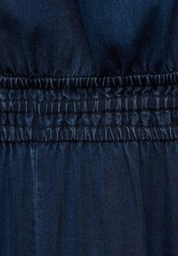 Tissu en denim bleu foncé avec couture élastique froncée créant une texture froncée horizontale.