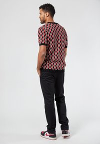 Suéter de manga corta en un patrón geométrico de negro, rojo y blanco; combinado con pantalones negros y zapatillas con acentos rojos. Cuello y puños acanalados.