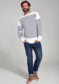 Hvid langærmet skjorte med marineblå striber, parret med mørkeblå jeans og brune snørebåndssko. Skjorten har en bådformet halsudskæring.