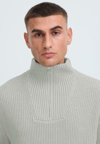 Helles graues geripptes Sweatshirt mit hohem Kragen und kurzem Reißverschluss. Verfügt über ein strukturiertes Muster und eine taillierte Passform.