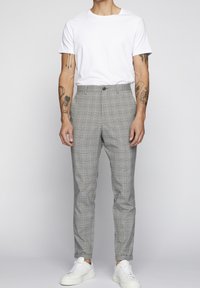 Grå rutiga byxor med en åtsittande design, med knappstängning och subtila blå detaljer, kombinerat med en enkel vit t-shirt och vita sneakers.