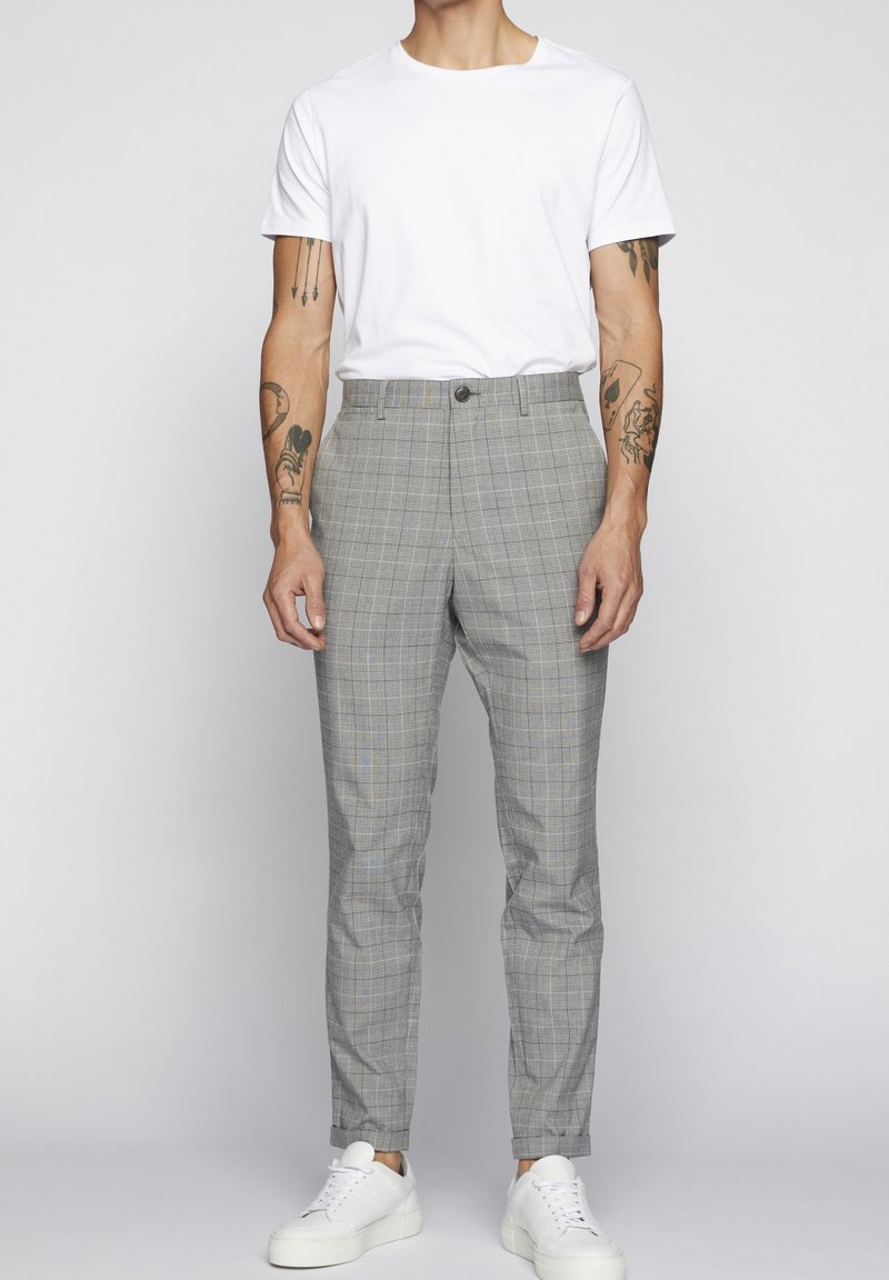 Grå rutiga byxor med en åtsittande design, med knappstängning och subtila blå detaljer, kombinerat med en enkel vit t-shirt och vita sneakers.