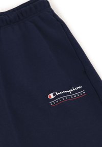 Joggers deportivos en azul marino hechos de algodón suave, con una cinturilla elástica y un logo "Champion" en blanco y rojo en el lado izquierdo.