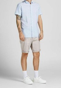 Světle modrá košile s krátkým rukávem a geometrickým vzorem, doplněná o vyhrnuté béžové šortky a bílé tenisky, vytvářející neformální vzhled.