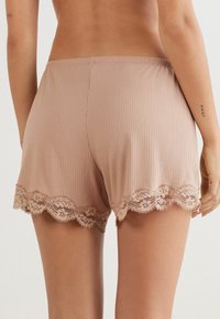 Nude ribbed shorts met een kanten rand langs de zoom. De stof lijkt zacht en heeft een licht rekbare textuur.