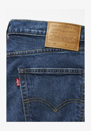Jean en denim de Levi Strauss & Co., avec une étiquette en cuir marron portant un logo en relief, un tissu bleu, des coutures dorées et un détail de languette rouge.