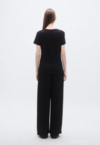 Črna bombažna majica s kratkimi rokavi in sproščenim krojem, kombinirana z širokimi črnimi hlačami. Gladek tekstura, minimalen dizajn.