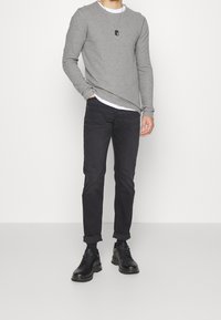 Szara koszula z długim rękawem, biała koszulka z okrągłym dekoltem pod spodem, połączona z czarnymi zwężanymi dżinsami i czarnymi sneakersami. Prosty, casualowy design i tekstury.