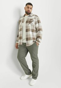 Geruite shirt in bruin en wit, met lange mouwen en twee voorzakken; gecombineerd met olijfgroene broek en witte sneakers.