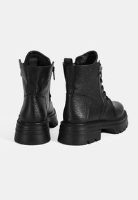 Bottes chelsea en cuir noir avec une finition texturée, laçage à l'avant, fermeture éclair sur le côté et semelle en caoutchouc épaisse pour la durabilité et l'adhérence.