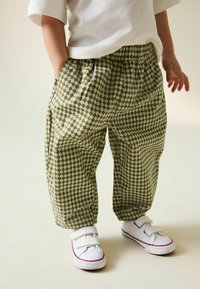 Grüne karierte Hose mit elastischem Bund, locker geschnitten und mit Seitentaschen, kombiniert mit weißen Turnschuhen mit roten Akzenten.