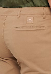 Béžové bavlněné kalhoty s zadní kapsou, na které je našita nášivka s nápisem "PS Paul Smith". Hladký povrch, rovný střih a minimální design.