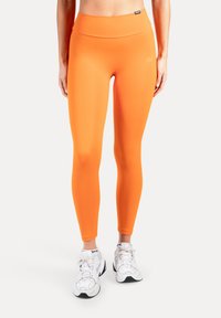 Orangea leggings med hög midja, slät och stretchig textur, figurnära design och en diskret logodetalj nära midjebandet, matchade med vita sneakers.