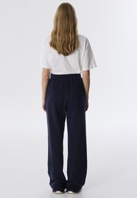 Wit oversized t-shirt en marineblauwe sweats met een gestructureerde zak, losse pasvorm, elastische tailleband en gerimpelde enkelmanchetten.