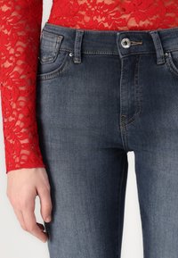 Los pantalones vaqueros de denim azul oscuro presentan un ajuste clásico con un diseño de cinco bolsillos, cierre de botón plateado y detalles de costura sutiles.