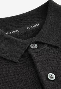 Svart stickad polotröja med krage, med två knappar och en skötsel etikett med texten "ALLSAINTS" på nacken. Mjuk textur.