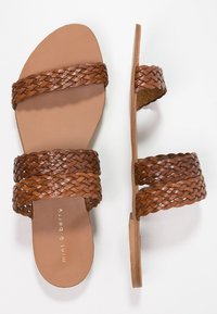 Sandali in pelle intrecciata marrone con suola piatta, design aperto sulla punta e fasce larghe. Superficie testurizzata con una fodera interna liscia.