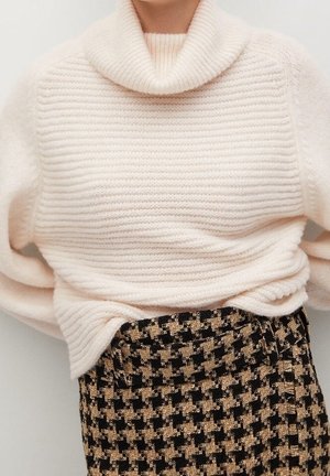 Femme portant un pull à col roulé côtelé crème rentré dans une jupe taille haute pied-de-poule noire et beige.