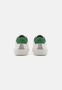 Valged sneakers roheliste kandekohustega, hall siidist detail, tekstureeritud kummitald ja mustriline brändi logo seljal.
