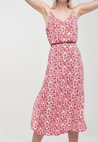 Robe imprimée florale rouge et blanche avec un décolleté en V, des fines bretelles et une taille cintrée. Le tissu a une texture douce et légère. Mi-longue.