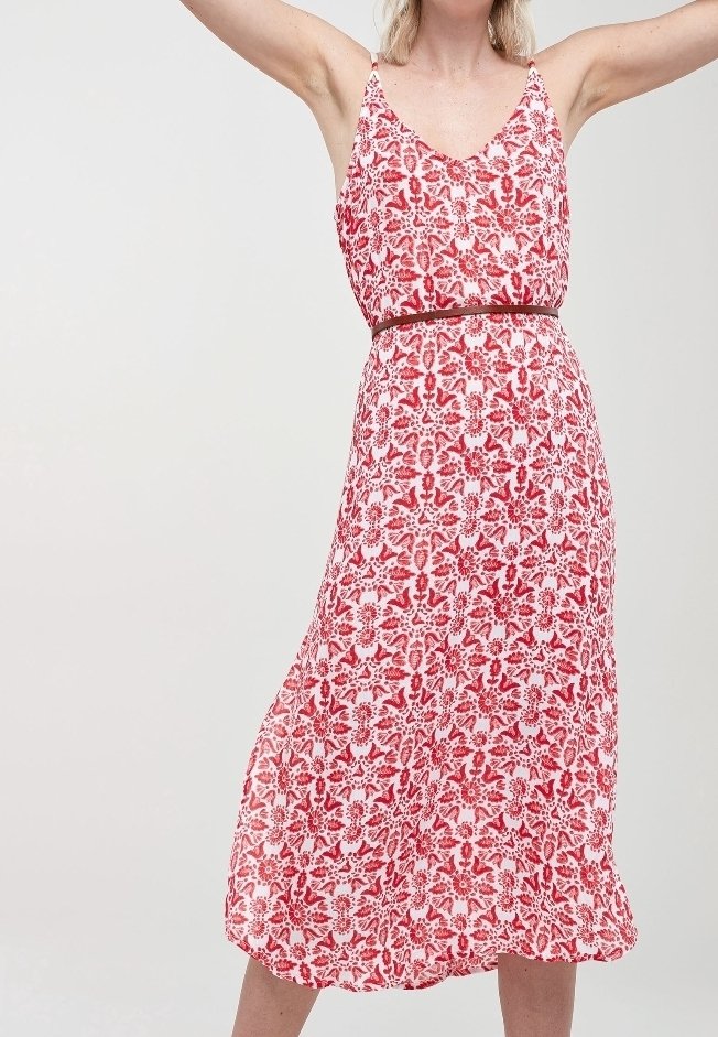 Robe imprimée florale rouge et blanche avec un décolleté en V, des fines bretelles et une taille cintrée. Le tissu a une texture douce et légère. Mi-longue.