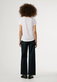 T-shirt blanc à manches courtes et jeans larges bleu marine. Les jeans ont une texture denim classique avec des coutures visibles et des détails de poche.