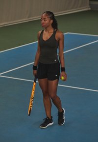 Tennisspiller iført en mørk ermeløs topp og svarte shorts, holder en oransje racket og en grønn tennisball, på en blå bane.