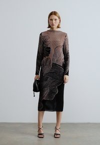 Robe rayée noire et rose avec un motif floral, manches longues, texture côtelée et silhouette droite. Accessoirisée avec un petit sac noir.