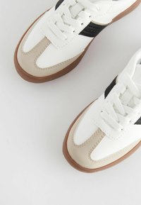 Białe sneakersy z brązowymi i czarnymi akcentami. Gładka skóra i zamszowe materiały. Projekt na sznurowanie z gumową podeszwą. Okrągły kształt palców.