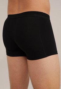 Črne bombažne boksarice z gladko teksturo, elastičnim pasom in detajli šivanja na straneh. Prilegajoča se zasnova, dolžina do sredine stegna.