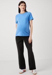 Blue cotton t-shirt with short sleeves, paired with black wide-leg pants. Model wears white sneakers with red accents. Simple, casual style.