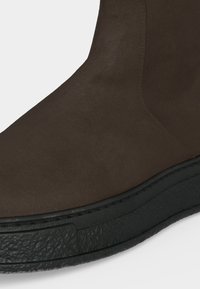 Κοντινό πλάνο καφέ σουέντ παπουτσιού με μαύρη υφασμάτινη λαστιχένια σόλα, παρουσιάζοντας λεπτομερή ραφή και λεία υφή σουέντ.