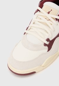 Izbliza bež i burgundski tenisica s materijalima od suede i mrežice, kremastožutim vezicama i potplatom s zračnim jastučićima na bijeloj pozadini.