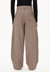 Weite Hosen aus einem strukturierten braunen Stoff mit hohem Bund und Gesäßtasche. Der Stoff hat ein dezentes Muster.