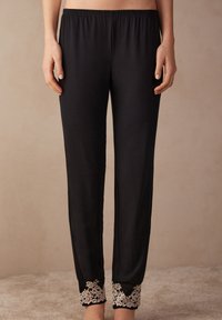 Zwarte pyjama broek met een elastische tailleband, voorzien van ingewikkelde witte kantdetails bij de enkels en een gladde, zachte textuur.