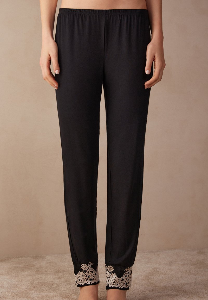 Zwarte pyjama broek met een elastische tailleband, voorzien van ingewikkelde witte kantdetails bij de enkels en een gladde, zachte textuur.