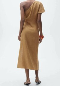 Asymmetrisches, einseitiges braunes Kleid aus strukturiertem Stoff, knielang mit fließender Silhouette, kombiniert mit einem orangefarbenen Armreif.