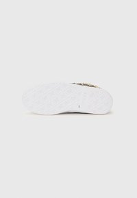 Hvit sneakersåle med teksturerte mønstre, preget logo og detaljerte designelementer. Glatt gummimateriale med flat form.