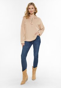 Felpa beige con patta a bottoni, vestibilità rilassata, abbinata a jeans skinny blu e stivaletti beige alla caviglia con dettagli perforati.