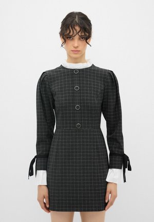 Black checkered dress with puffed long sleeves, featuring four circular buttons and white ruffled collar and cuffs. Black ribbon accents at sleeves.