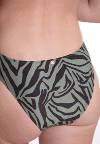 Hoog-waisted bikini broekje in olijfgroen met zwarte zebra-stripes. Voorzien van een metallic accentlabel en een textuurstof.