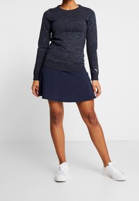 Navy long-sleeve knit top with a crew neck, paired with a dark navy skort. White athletic sneakers complete the outfit.