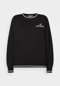 Svart sweatshirt med långa ärmar, rund halsringning, vitt randigt detaljer vid hals och muddar, samt "Hollister"-logotypen framtill.