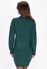 Abito maglione teal con maniche lunghe, silhouette aderente e dettagli in paillettes lungo le spalle. Texture morbida, polsini a coste.