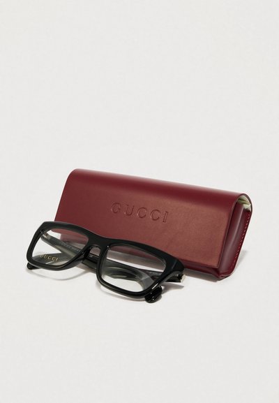 Zwarte rechthoekige bril met heldere lenzen, geplaatst naast een kastanjebruine leren etui met het opschrift "GUCCI." Gladde textuur, geen zichtbare patronen.