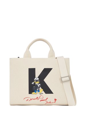 Sac en toile crème avec un grand "K" noir, mettant en scène un personnage de dessin animé en tenue noire, accompagné de détails de signature en texte rouge.