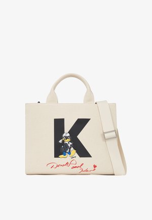 Canvas-Handtasche in Creme mit einem großen schwarzen "K". Sie zeigt eine Cartoonfigur in einem schwarzen Outfit, begleitet von rot eingefärbten Unterschrift-Details.