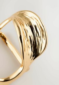 Gold-toned cuff bracelet with a wavy, textured surface, featuring smooth and polished accents for a reflective finish.