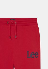 Czerwone bawełniane dresy z elastycznym pasem, regulowanym sznurkiem i granatowym logo "Lee" na lewym nogawce. Gładka tekstura.