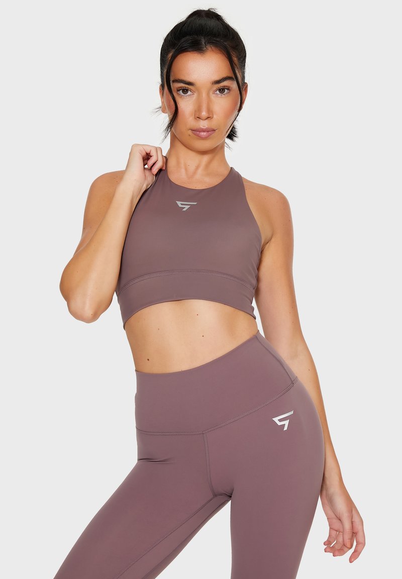 Mauve sportbeha met ronde halslijn en logo, gecombineerd met high-waisted leggings met een zijnaad en logoaccent. Gladde textuur.